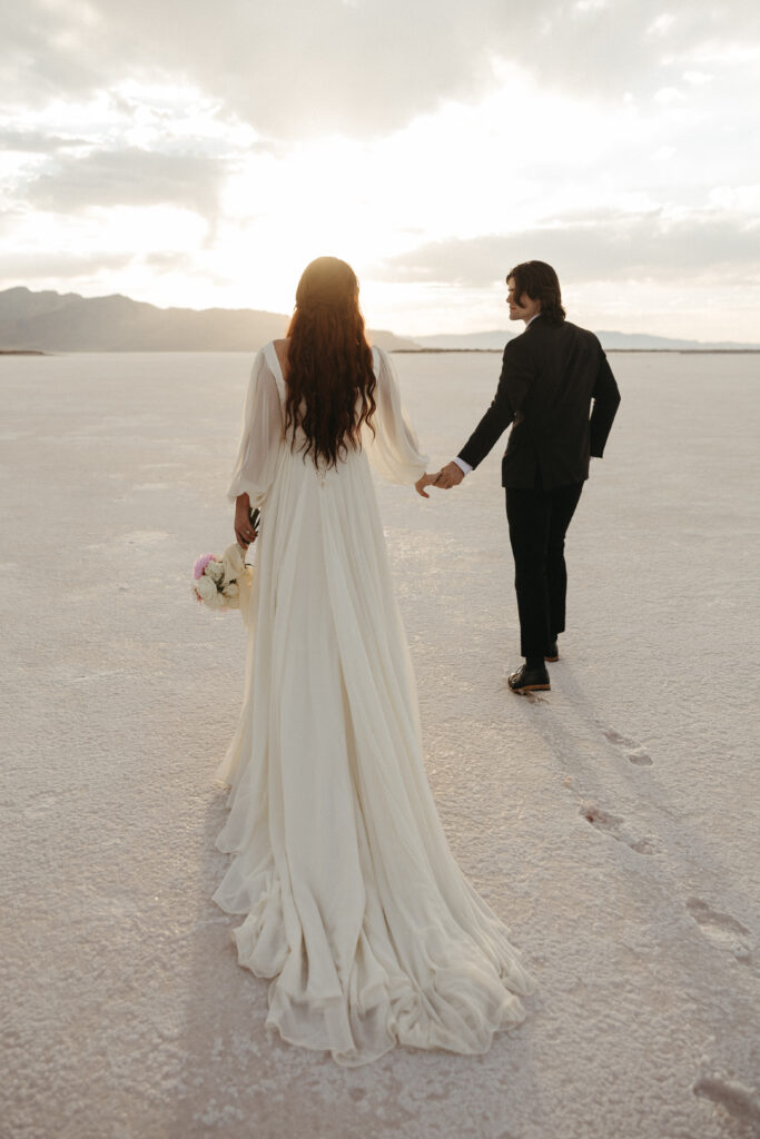 Bride and groom walking into the sunset after eloping at Bonneville Salt Flats in Utah.